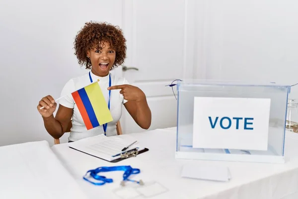 Young african american woman at political campaign election holding colombia flag smiling happy pointing with hand and finger