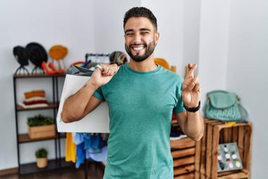 Satış mağazasında sakallı, alışveriş torbası tutan genç yakışıklı adam umut ve gözlerin kapalı bir şekilde gülümseyerek el kol geziyor. Şans ve batıl inançlar. 