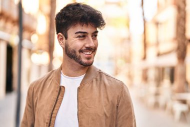 Young hispanic man smiling confident looking to the side at street