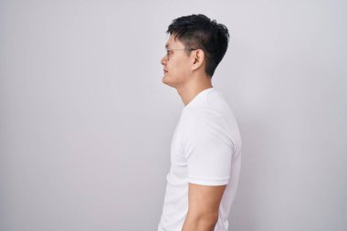 Young asian man standing over white background looking to side, relax profile pose with natural face and confident smile. 