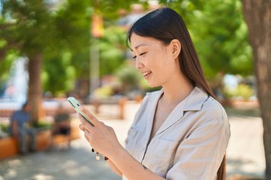 Parkta akıllı telefon kullanan, kendine güvenen Çinli bir kadın.