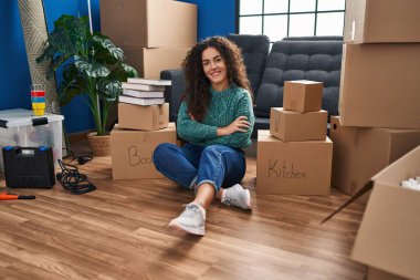 Genç, güzel, kendine güvenen İspanyol bir kadın yeni evinde kollarını kavuşturup oturuyor.