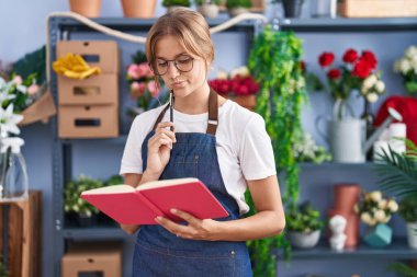 Young blonde girl florist reading book with doubt expression at florist