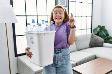 Geri dönüşüm sepetini elinde tutan, elinde plastik şişelerle el sallayan genç kızıl saçlı kadın umut ve gözlerle gülümsüyor. Şans ve batıl inançlar. 