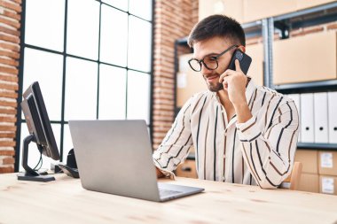 Genç İspanyol iş adamı. Ofiste bilgisayarla akıllı telefondan konuşuyor.
