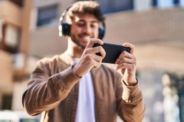 Young hispanic man smiling confident playing video game at street