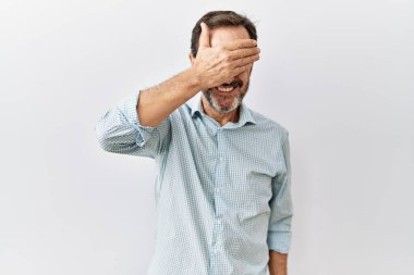 Orta yaşlı, sakallı, soyutlanmış arka planda dikilen, gülümseyen ve yüzünde şaşkınlıktan gözleri kapayan İspanyol bir adam. kör kavram. 