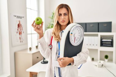 Elinde tartı makinesi ve yeşil elma tutan genç sarışın kadın üzgün ve endişeli, sinirli ve korkmuş bir şekilde ağlıyor. hüzünlü ifade. 