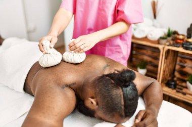 Young african american man having back massage with thai bags at beauty center