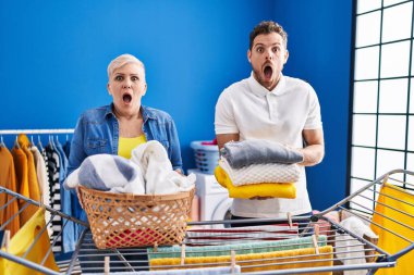 Hispanic mother and son hanging clothes at clothesline afraid and shocked with surprise and amazed expression, fear and excited face. 