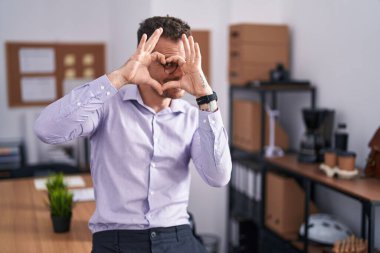 Ofisteki genç İspanyol adam kalp şeklinde elleriyle ve parmaklarıyla tabelanın içinden bakıp gülümsüyor. 