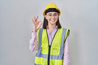 Hispanic girl wearing builder uniform and hardhat smiling positive doing ok sign with hand and fingers. successful expression. 