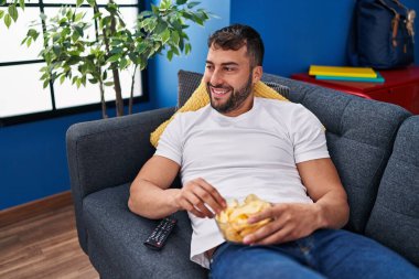 Evdeki kanepede uzanmış film izleyen İspanyol genç adam.