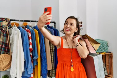Orta yaşlı İspanyol kadın gülümsüyor. Satış mağazasında akıllı telefonuyla selfie çekiyor.