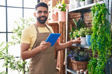 Young arab man florist smiling confident using touchpad at florist