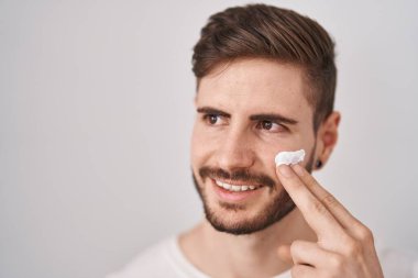 Sakallı İspanyol adam nemlendirici yüz kremi kullanıyor. Gülümsüyor ve başka tarafa bakıyor.. 