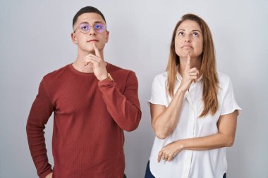 Anne ve oğlu izole bir arka planda bir arada duruyorlar şüphe üzerine yoğunlaşmışlar, parmakları çenelerinde ve yukarı bakıp merak ediyorlar. 