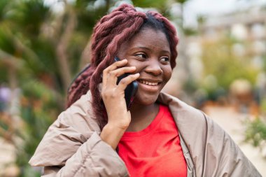 Afro-Amerikalı kadın gülümsüyor. Parktaki akıllı telefondan konuşuyor.