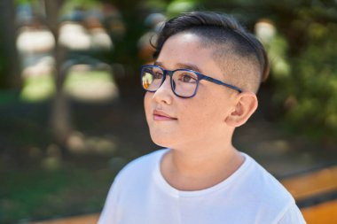 Sevimli İspanyol çocuk, gülümsüyor. Parkta kendinden emin bir şekilde yan tarafa bakıyor.