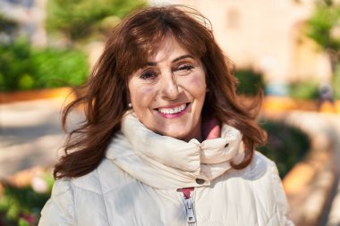 Orta yaşlı bir kadın parkta kendine güvenerek gülümsüyor.