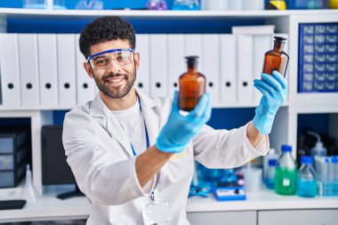 Laboratuvarda elinde şişe tutan bilim adamı üniforması giyen genç bir Arap.