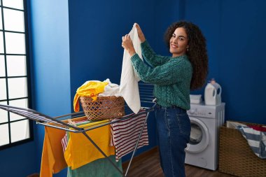 Genç ve güzel İspanyol kadın gülümsüyor çamaşırhanede çamaşır ipine asılan kendine güvenen kıyafetler.