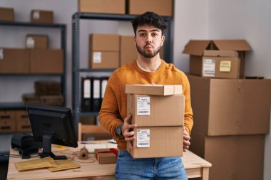 Küçük işletme şirketinde sakallı İspanyol bir adam elinde paketler tutarak komik yüzlü yanakları şişiriyor. Ağzı havayla şişer, havayı yakalar.. 