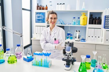 Bilim adamı üniforması giyen genç bir kadın laboratuarda kameraya bakıyor.