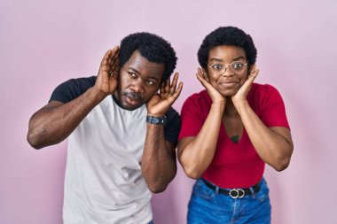 Genç Afro-Amerikan çifti pembe arka planda dikilip iki elini de dedikodu meraklısı kulak hareketlerini duymaya çalışıyor. İşitme sorunu, sağır 