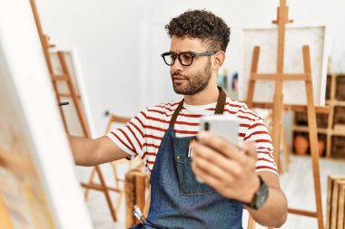 Sanat stüdyosunda akıllı telefon çizimi yapan genç bir Arap sanatçı..