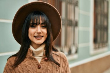 Açık havada gülümseyen, kışlık şapkalı esmer kadın.