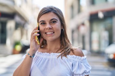 Gülümseyen genç bir kadın caddedeki akıllı telefondan konuşuyor.