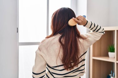 Young hispanic woman combing hair at home