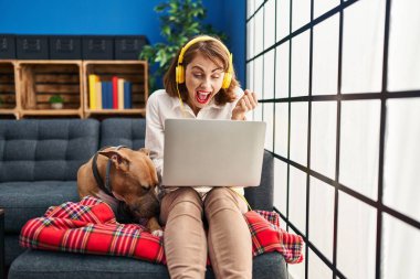 Dizüstü bilgisayar kullanan genç ve güzel bir kadın gururla bağırıyor, zaferi kutluyor ve kollarını kaldırarak heyecanlanıyor. 