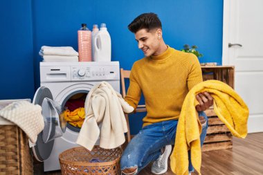 Genç İspanyol adam gülümsüyor çamaşırhanede çamaşır yıkıyor.