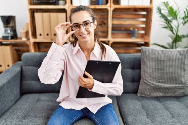 Young hispanic woman smiling confident having psychologist session at clinic