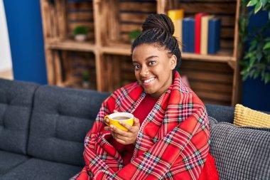 African american woman drinking coffee sitting on sofa at home
