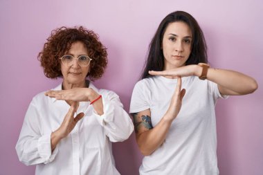 İspanyol anne ve kızı pembe arka planda günlük beyaz t-shirt giyiyorlar. Elleriyle hareket ediyorlar, hayal kırıklığına uğramış ve ciddi bir yüz ifadesiyle. 