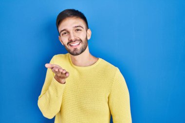 Mavi arka planda durup gülümseyen İspanyol bir adam. Neşeli bir şekilde yardım eli uzatıyor ve kabul ediyor.. 
