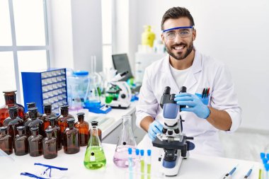 Yakışıklı İspanyol adam, bilim adamının laboratuarında çalışıyor. Olumlu ve mutlu görünüyor. Kendine güvenen bir gülümsemeyle dişlerini gösteriyor. 