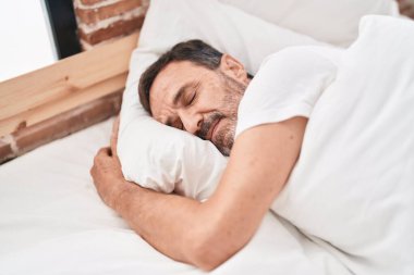 Orta yaşlı bir adam yatakta uzanıyor, yatak odasında uyuyor.