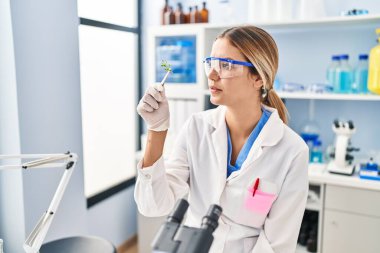 Genç İspanyol bilim kadını laboratuvarda bitki örneğini cımbızla tutuyor.