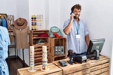 Genç İspanyol esnaf gülümsüyor. Giyim mağazasında çalışan akıllı telefondan konuşuyor..