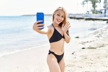 Young cuacasian girl wearing bikini having video call using smartphone at the beach.