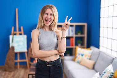 Sarışın, beyaz bir kadın oturma odasında duruyor. Gülümsüyor, kameraya göz kırpıyor ve zafer işareti yapıyor. İki numara.. 