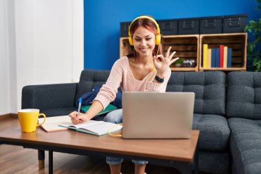 Bilgisayar laptopu kullanan beyaz bir kadın parmaklarıyla imza atıyor, gülümsüyor ve mükemmel bir sembol oluşturuyor. 