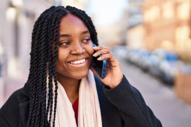 Afro-Amerikalı kadın gülümsüyor. Akıllı telefondan konuşuyor.