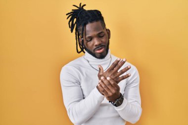 Sarı arka plan üzerine balıkçı yaka kazak giyen Afrikalı bir adam ellerinde ve parmaklarında ağrı, iltihaplanma 