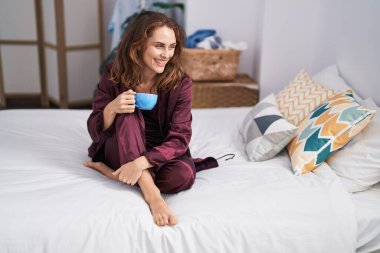 Genç bir kadın yatak odasında bir fincan kahve içiyor.