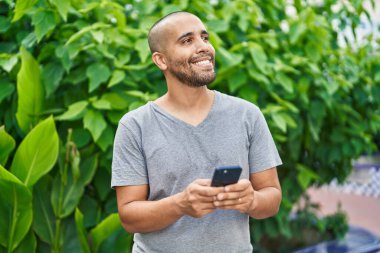 Parkta akıllı telefon kullanarak gülümseyen genç Latin adam.